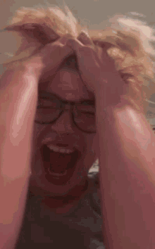 a man wearing glasses is laughing and holding his head