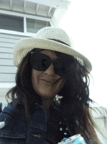 a woman wearing a straw hat and sunglasses is holding a can of soda