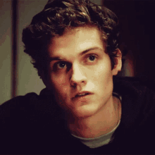 a young man with curly hair looks at the camera with a serious look on his face