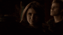 a woman in a dark room looks at a man