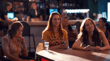 three women are sitting at a table with one wearing a yellow shirt that says love more