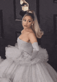 a woman in a white dress and white gloves stands in front of a grammy statue