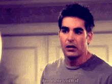 a man in a gray shirt is saying `` i 'm done with it '' while standing in front of a door .