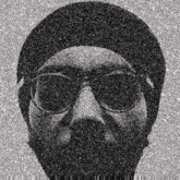a black and white photo of a man with a beard wearing glasses and a hat .
