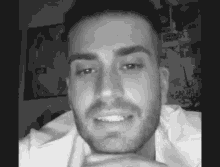 a black and white photo of a man with a beard smiling with his hand on his chin .