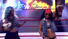 two women are standing in a wrestling ring holding championships