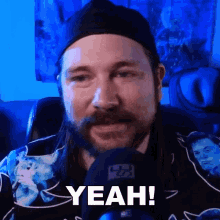 a man with a beard is wearing a black hat and a shirt that says yeah