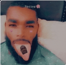 a man with a beard is laying on a bed with his tongue sticking out and a sticker on his face .
