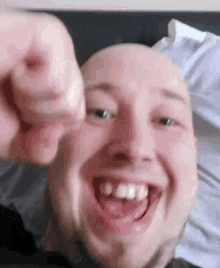 a bald man with a beard is smiling and pointing at the camera while laying on a bed .