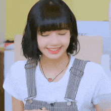 a young woman wearing overalls and a white shirt is smiling .
