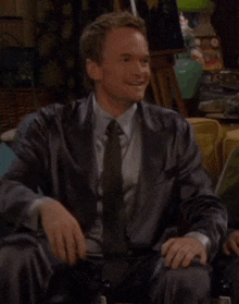 a man in a suit and tie says come on guys i 'm carrying the team while sitting on a couch