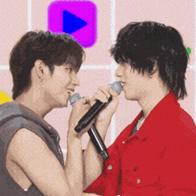 two young men singing into microphones in front of a pink play button
