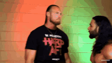 a man wearing a shirt that says hard af stands next to another man