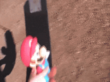 a mario figure is sitting on a skateboard on a dirt surface
