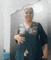 an older woman wearing a blue floral embroidered top is standing in front of a wardrobe .