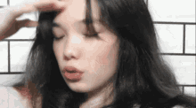 a woman with long black hair is touching her forehead .