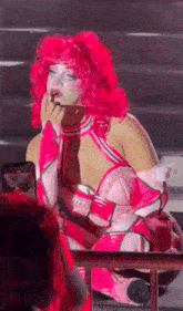 a drag queen with pink hair is sitting on the stage