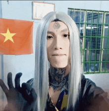 a man with long white hair and a tattoo on his forehead is giving the ok sign