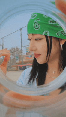 a woman wearing a green bandana is looking through a glass