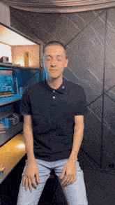 a man wearing a black polo shirt is sitting in front of a bookshelf with his eyes closed