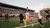 a football player is running on a field with a stadium in the background that says " trophy room "