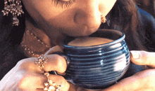 a woman with rings on her fingers drinking from a blue cup