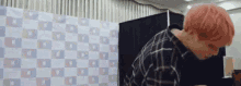 a man with pink hair is sitting in front of a checkered wall .