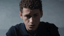 a young man with curly hair wearing a blue shirt