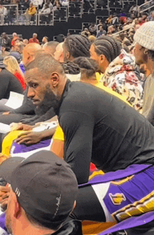 lebron james sits in the stands at a basketball game wearing a lakers jersey