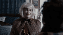 a woman in a fur coat is talking to a man in a bedroom .