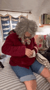 a woman with gray hair and glasses is sitting on a bed looking at something