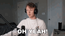 a young man wearing headphones is sitting in front of a microphone and saying oh yeah .
