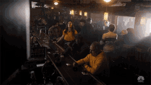 a group of people are sitting at a bar drinking beer and smoking cigarettes .