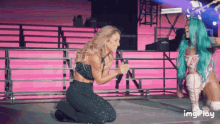 a woman with green hair is kneeling down next to another woman on a stage and the words imgplay are on the bottom