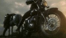 a man is riding a motorcycle next to a horse in a field .