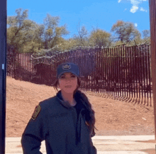 a woman standing in front of a barbed wire fence wearing a hat that says border patrol on it