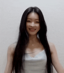 a woman with long black hair is wearing a white tank top and smiling at the camera .