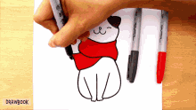 a person is drawing a cat wearing a red scarf on a piece of paper that says drawbook
