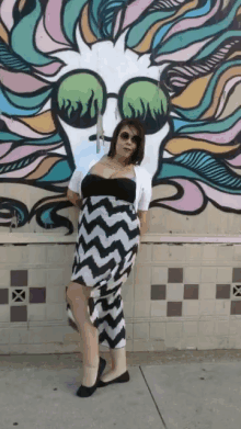 a woman wearing sunglasses stands in front of a colorful mural of a skull