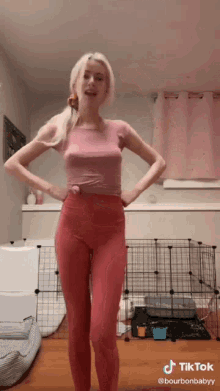 a woman wearing pink leggings and a pink shirt is standing in a room with her hands on her hips