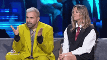 a man in a yellow suit is sitting next to a woman in a black vest