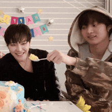 two boys are sitting at a table with a cake and a banner that says 99ah on it
