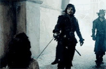 a man in a black coat is holding a sword while walking down a street .