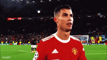 a soccer player in a red adidas jersey stands on the field