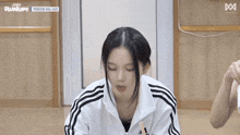 a woman wearing a white adidas jacket is sitting on the floor