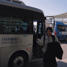 a woman standing in front of a bus with the number 1544-8963 on the side