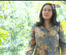 a woman in a floral shirt stands in front of trees with the number 3 on the bottom