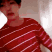 a man wearing a red striped shirt is standing in front of a window .