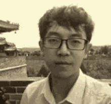 a black and white photo of a young man wearing glasses and a white shirt .