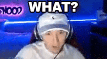 a man wearing headphones and a hat is sitting in front of a computer screen and says `` what ? ''
